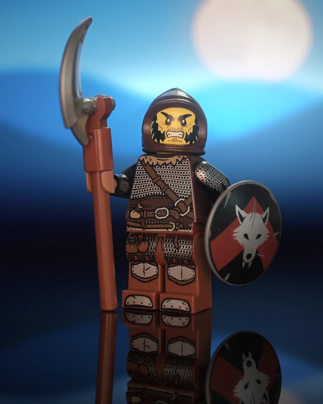 Castle Clad Bricks pad-printed Wolfpack minifig in a dark-brown farmer's cowl, with yellow head, wild frown, black mutton chops and stub mustache. Dark-brown torso with dark-tan fur collar, dagged chainmail and medium-brown strap and belt; black arms with chainmail and splinted forearms. Reddish-brown legs with mail skirt, loot bags, iron-clad feet and medium-brown trimmed knee guards. Holds a pole-axe and a dark-bluish-gray round shield with a silver wolf head on a red upward chevron over black.